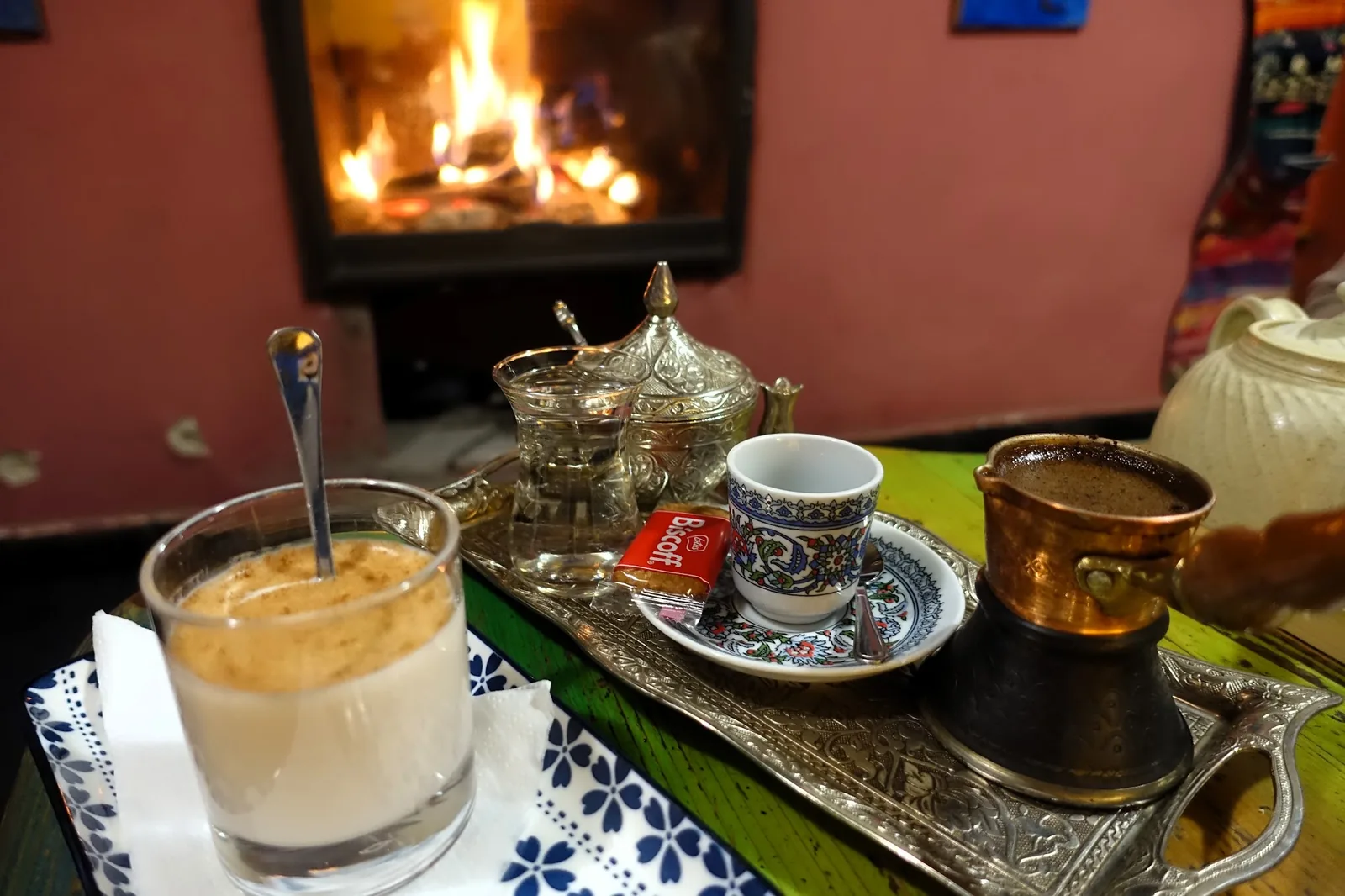 Strieborný podnos s džezvou a arabskou kávou pred horiacim krbom